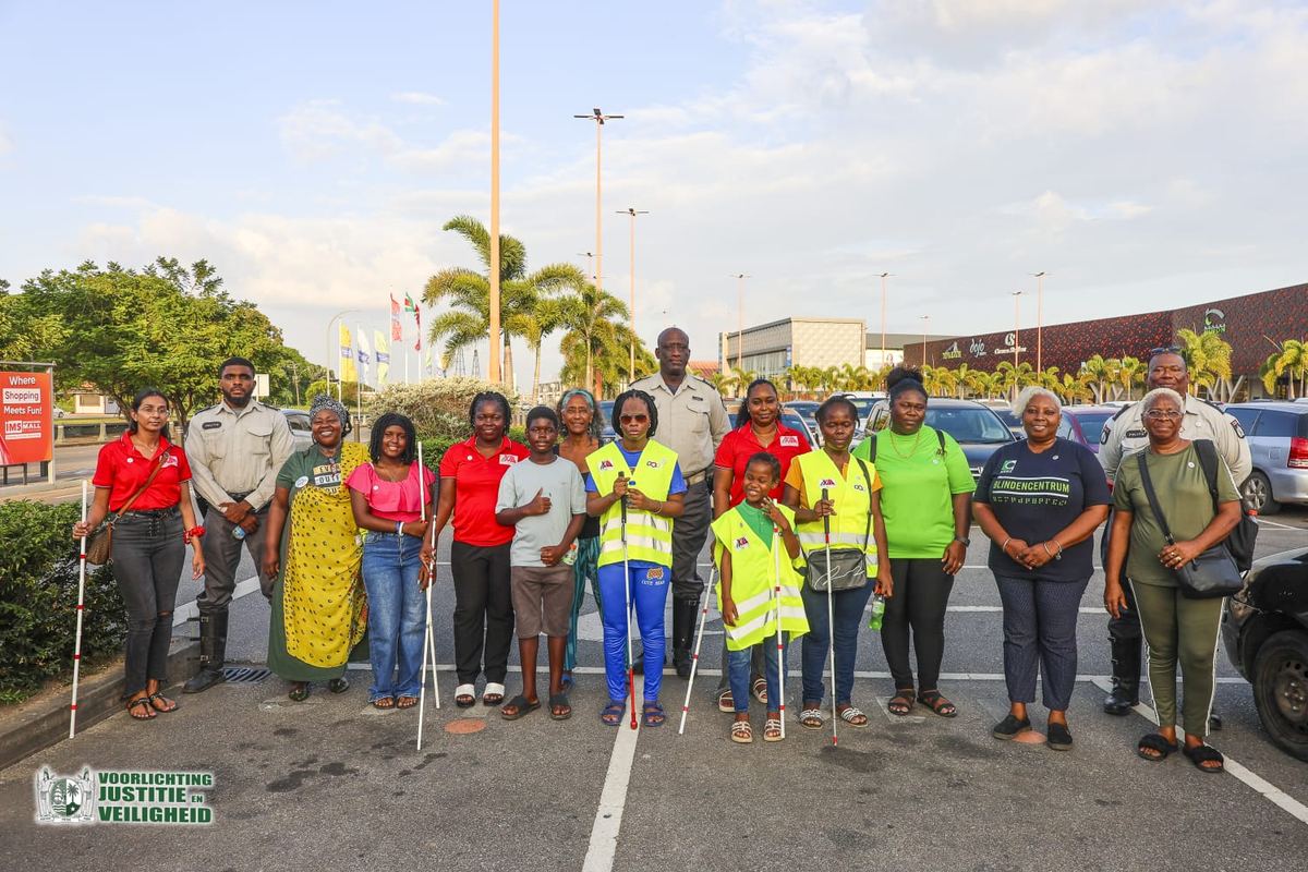 Deelnemers van het Blindencentrum, het VVI, het KSV en het Korps Politie Suriname met witte blindenstokken op een parkeerterrein